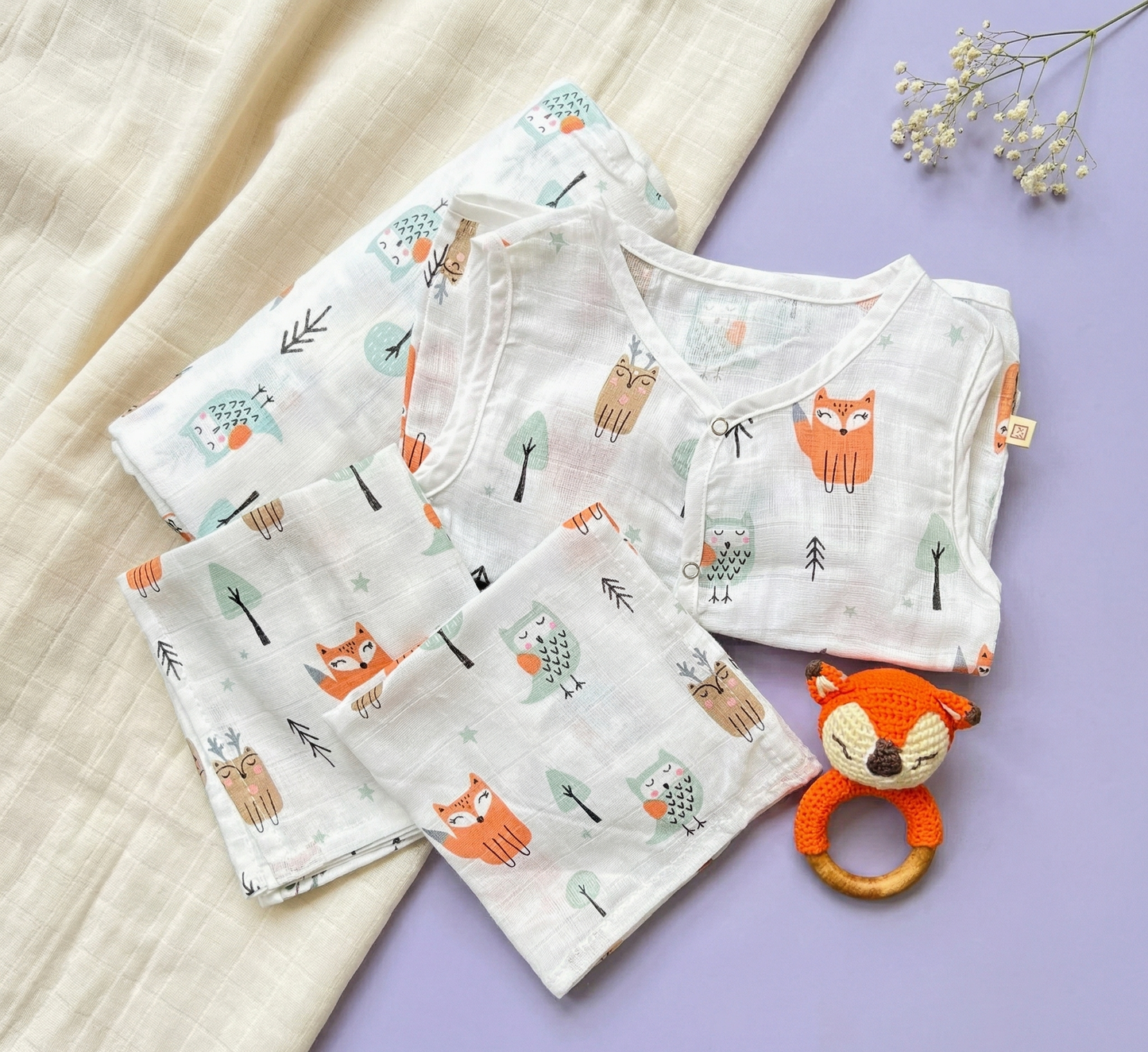 Baby clothing set with fox patterns on a light purple surface, accompanied by a fox-themed rattle.